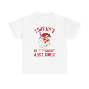 May include: White t-shirt with a vintage Santa Claus graphic. The Santa illustration is wearing a red hat and has a white beard. The text on the shirt reads "I GOT HO'S IN DIFFERENT AREA CODES" in red letters.