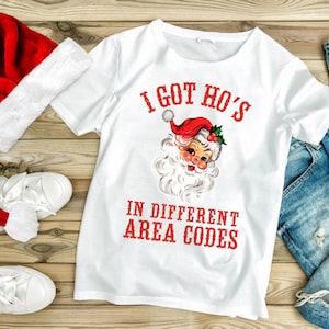 May include: White t-shirt with a red and white illustration of Santa Claus and the text "I got ho's in different area codes".