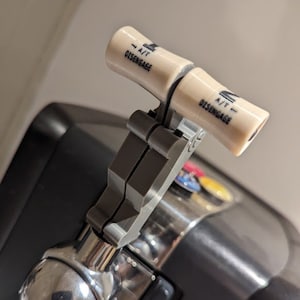 Puede incluir: Primer plano de un grifo de cerveza plateado con una palanca negra y gris. La palanca tiene dos botones blancos que dicen "A/T - DISENGAGE".