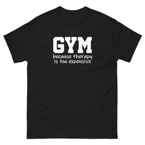 Op de afbeelding: Zwart T-shirt met witte tekst die "GYM omdat therapie te duur is" zegt.