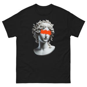 Peut inclure: Un t-shirt noir avec une sculpture de buste de femme blanche avec une couronne de laurier sur la tête. Les yeux de la femme sont recouverts d'une éclaboussure de peinture orange vif.