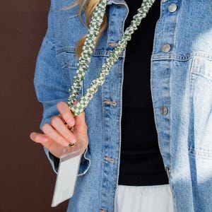 May include: A green and white checkered lanyard with a clear plastic ID holder. The lanyard is worn over a denim jacket and black top. The ID holder is empty. The lanyard is made of a soft, woven material.