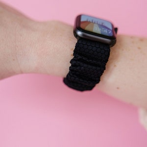 May include: A black Apple Watch with a black honeycomb patterned band. The watch face displays a colorful design and the time 12:47.
