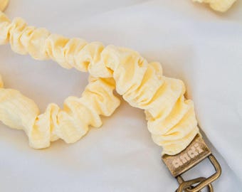 May include: A light yellow fabric lanyard with a textured, gathered design. The lanyard has a bronze-colored metal clasp and key ring. The fabric is a soft, pastel yellow color.