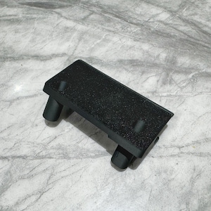 Pode incluir: Um apoio para os pés retangular preto com uma superfície texturizada e quatro pernas cilíndricas. O apoio para os pés foi projetado para elevar os pés e proporcionar conforto. O produto é feito de um material durável.