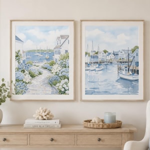 May include: Two framed watercolor prints depicting coastal scenes. The left print shows a stone path lined with blue and white hydrangeas leading to a harbor with sailboats. The right print features a harbor with docked boats and waterfront houses.