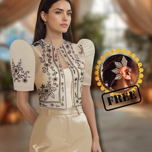May include: Cream-colored, embroidered top with puff sleeves and matching pants. The top features black floral embroidery. A gold ear cuff with a sunburst design is also visible. The word "FREE" is stamped on the image.