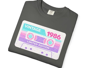 Könnte beinhalten: Dunkelgraues T-Shirt mit einem Retro-Kassettenband-Design. Das Design enthält die Worte "VINTAGE 1986 LIMITED EDITION" in einem türkis-, rosa- und lilafarbenen Farbschema. Das Shirt ist aus einem weichen Material.
