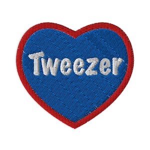 Pode incluir: Um remendo em forma de coração vermelho com um centro azul e a palavra "Weezer" bordada em branco.