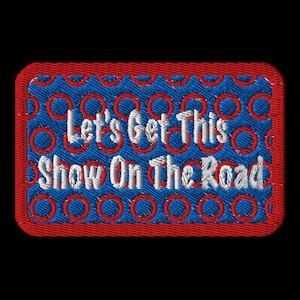 May include: Red and blue embroidered patch with a white background. The patch has a circle pattern and says "Let's Get This Show On The Road".