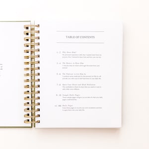 May include: A close-up of a table of contents page from a journal titled "The Podcast to Let Him In". The page lists the different sections of the journal, including "Why Hear Him?", "The Basics to Hear Him", "Open Your Heart and Mind Meditation", "Sample Daily Pages", and "Daily Pages".