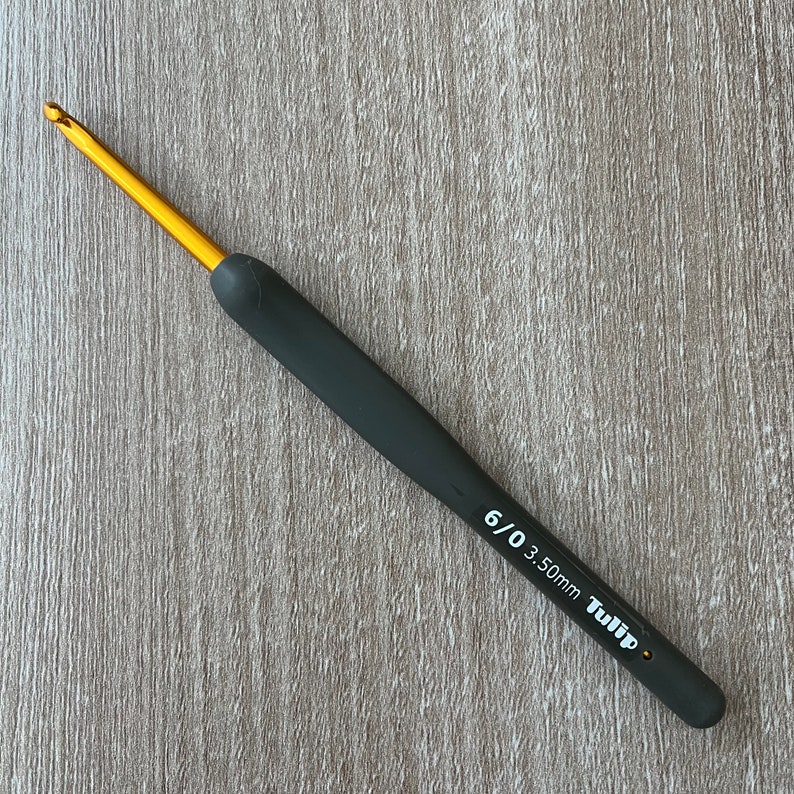Puede incluir: Un ganchillo negro y dorado con mango negro y punta dorada. El ganchillo est&aacute; etiquetado como "6/0 3.50mm Tulip".