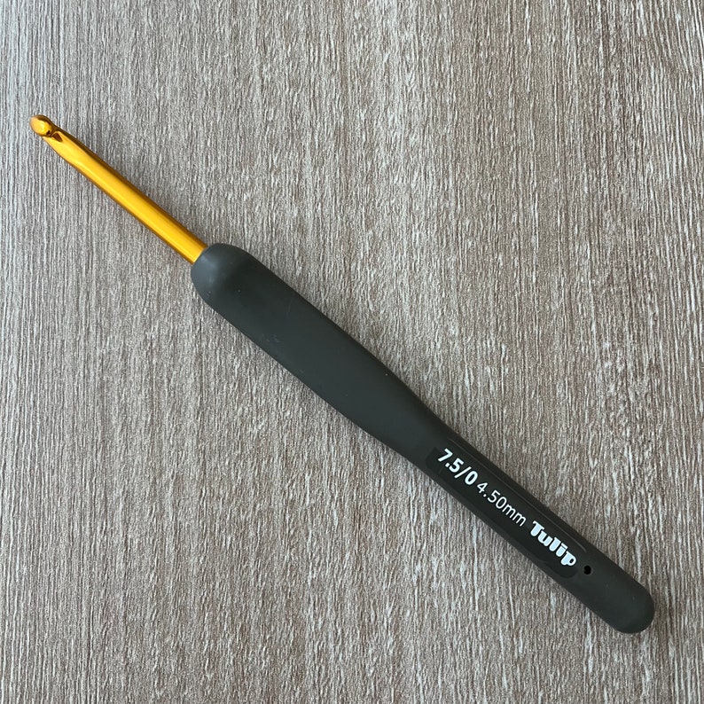 Puede incluir: Un ganchillo negro y dorado con mango negro y punta dorada. El ganchillo est&aacute; etiquetado con "7.5/0 4.50mm Tulip".