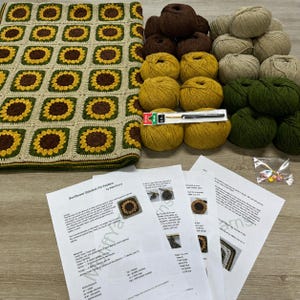 Puede incluir: Una manta de ganchillo con motivo de girasol en marrón, amarillo y crema, acompañada de varios ovillos de lana en colores a juego, un ganchillo de 4,0 mm, marcadores de puntos e instrucciones impresas tituladas Sunflower Blanket.