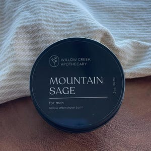 May include: A dark blue round tin of Mountain Sage tallow aftershave balm from Willow Creek Apothecary. The label includes the text "for men" and the volume is 60 ml.