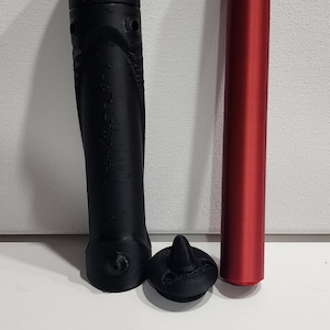 May include: A black lightsaber hilt with a red lightsaber blade. The hilt has a textured surface and a small, black cap on the end. The blade is approximately 45 cm long.