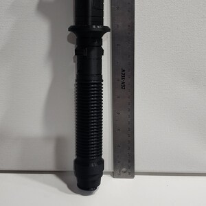 May include: A black 3D printed lightsaber prop, approximately 11 inches long, with a ribbed handle and a detailed hilt. The prop is next to a ruler for scale.