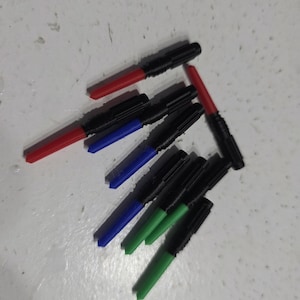 Pu&ograve; includere: Una collezione di pennarelli neri con punte colorate. Le punte sono rosse, blu e verdi. I pennarelli sono disposti su una superficie chiara.