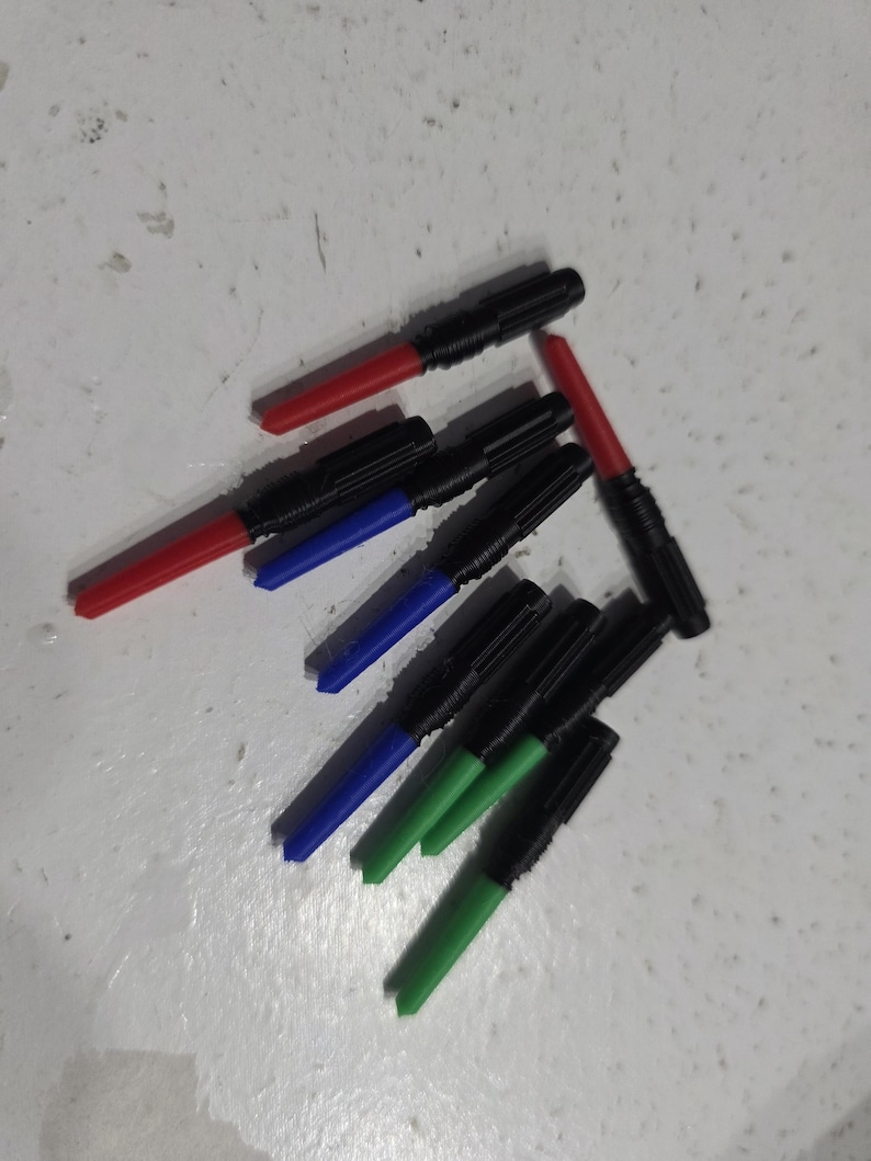 Pu&ograve; includere: Una collezione di pennarelli neri con punte colorate. Le punte sono rosse, blu e verdi. I pennarelli sono disposti su una superficie chiara.