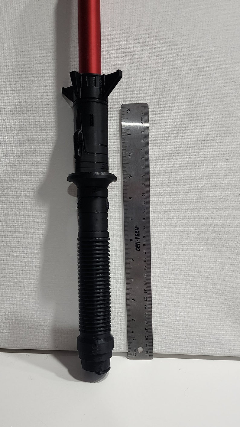 May include: A black lightsaber hilt with a red blade, measuring approximately 12 inches in length. The hilt has a textured grip and a metal ring near the top.