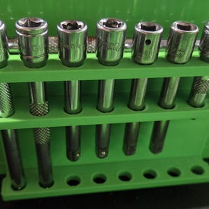 May include: A set of chrome sockets and a ratchet wrench are displayed in a bright green holder. The sockets are arranged in two rows, with the ratchet on the left. The tools are for mechanical work.