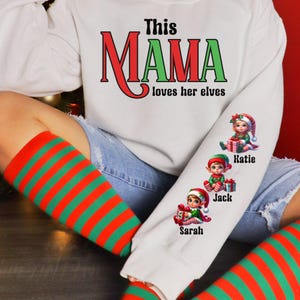 May include: White sweatshirt with the text "This MAMA loves her elves" in red and green. The sleeve features three elf illustrations with the names Katie, Jack, and Sarah. The person is wearing red and green striped socks.