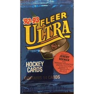 Puede incluir: Un paquete de cartas de hockey Fleer Ultra 1992-93 azul y amarillo con un disco de hockey negro y plateado y un círculo rojo con el texto "Collect Jeremy Roenick and "Award Winners" Limited Edition Subsets. Details on back." El paquete contiene 14 cartas.