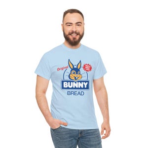 May include: A light blue short-sleeve t-shirt featuring a graphic of a rabbit head above the text "BUNNY BREAD" in blue and white. The design includes the red text "Original" and a red starburst shape with the text "THAT'S WHAT I SAID".