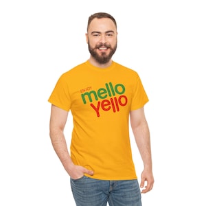 Puede incluir: Una camiseta amarilla con la frase "Enjoy Mello Yello" en verde y rojo. La camiseta de manga corta está hecha de un material suave. La persona lleva vaqueros azules.