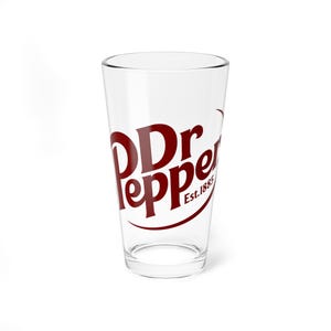 Puede incluir: Vaso de pinta transparente con el logotipo de Dr Pepper en rojo oscuro. El logotipo incluye las palabras "Dr Pepper" en una fuente estilizada, con "Est. 1885" debajo. El vaso está vacío y sobre una superficie blanca.