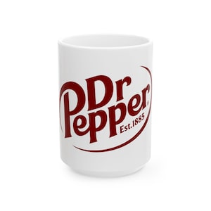 May include: White ceramic mug featuring the Dr Pepper logo in a bold, maroon color. The logo includes the words "Dr Pepper" in a stylized font, with "Est. 1885" below. The mug is cylindrical with a rounded base.