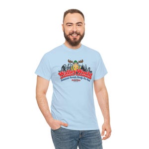 Op de afbeelding: Lichtblauw T-shirt met het "Walley World" logo, een cartoon eland en een achtbaan ontwerp. De tekst luidt "America's Favorite Family Fun Park" en "Stillness".
