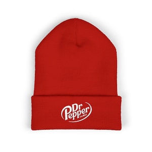 Może przedstawiać: Gładka czerwona czapka z białym logo Dr Pepper na złożonym brzegu. Logo przedstawia nazwę marki w stylizowanej czcionce ze słowami "Est. 1885" poniżej. Czapka wykonana jest z miękkiego, dzianinowego materiału.
