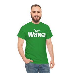 May include: A bright green short-sleeved t-shirt featuring the white text Wawa printed across the chest. Above the text is a white graphic of a flying goose. The shirt has a crew neckline and a standard fit, providing a simple and clean look.