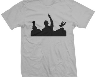 Può includere: Una maglietta grigia con una silhouette nera di una band che suona sul palco. I membri della band sono in silhouette su uno sfondo scuro.