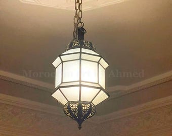 May include: A decorative pendant light with a geometric design. The light has a white, rectangular shade within a black metal frame. It hangs from a chain attached to a ceiling fixture.