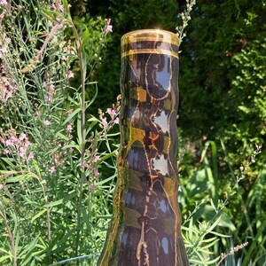 Puede incluir: Un jarrón de cerámica negro con un borde dorado y un diseño ondulado y texturizado. El jarrón está sobre una superficie de vidrio.