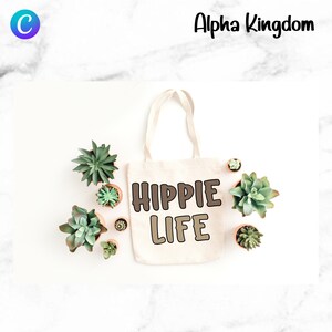 May include: A white canvas tote bag with the text "HIPPIE LIFE" in brown and beige letters. The bag is surrounded by small potted succulents on a white marble surface.