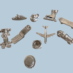Könnte beinhalten: Eine Sammlung von zehn silberfarbenen Spielsteinen aus Metall in verschiedenen Formen, darunter ein Rennwagen, ein Schiff, ein Zylinder, ein Mobiltelefon, ein Flugzeug, ein Skateboard, ein Stiefel, ein kreisförmiges Objekt und ein Oldtimer.
