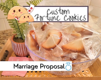 May include: A clear glass bowl filled with custom fortune cookies, each individually wrapped. The text "Custom Fortune Cookies" and "Marriage Proposal" are displayed. A small potted plant and a wooden tray are also visible.