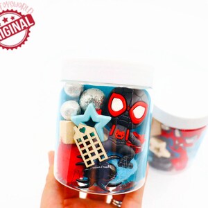 May include: A clear plastic jar filled with blue and red play dough, silver and white glitter balls, a small wooden house, a blue star, and a black and red Spider-Man figurine.