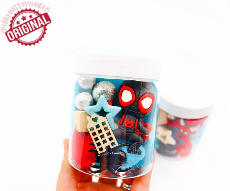 May include: A clear plastic jar filled with blue and red play dough, silver and white glitter balls, a small wooden house, a blue star, and a black and red Spider-Man figurine.