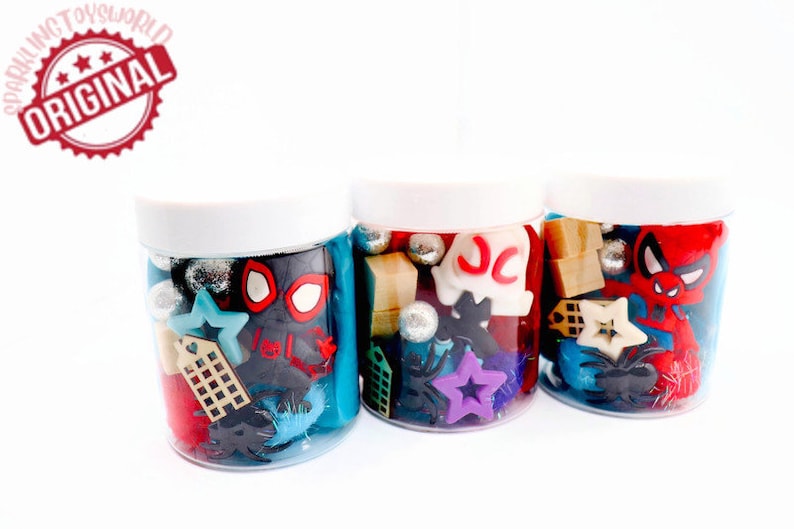 May include: Three clear plastic jars filled with colorful toy charms and beads. The jars have white lids. The charms include a red and black Spiderman figure, a white ghost with the letters "JC" on it, and a red and black Spiderman figure.