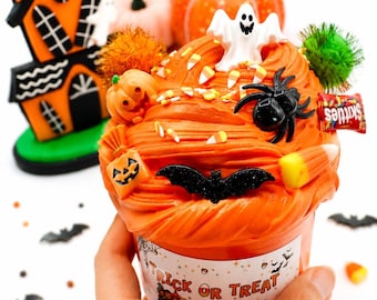 May include: An orange slime container topped with a white ghost, a black spider, a black bat, a small pumpkin, candy corn, and a Skittles packet. The label on the container features the text TRICK OR TREAT and SPARKLINGTOYSWORLD in black.