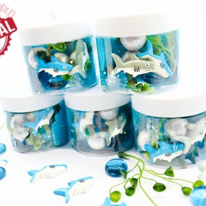 May include: Several clear plastic jars with white lids, filled with blue liquid, toy sharks, and decorative elements. The jars are arranged in a stack. The image includes the text "SPARKLING TOYSWORLD ORIGINAL".