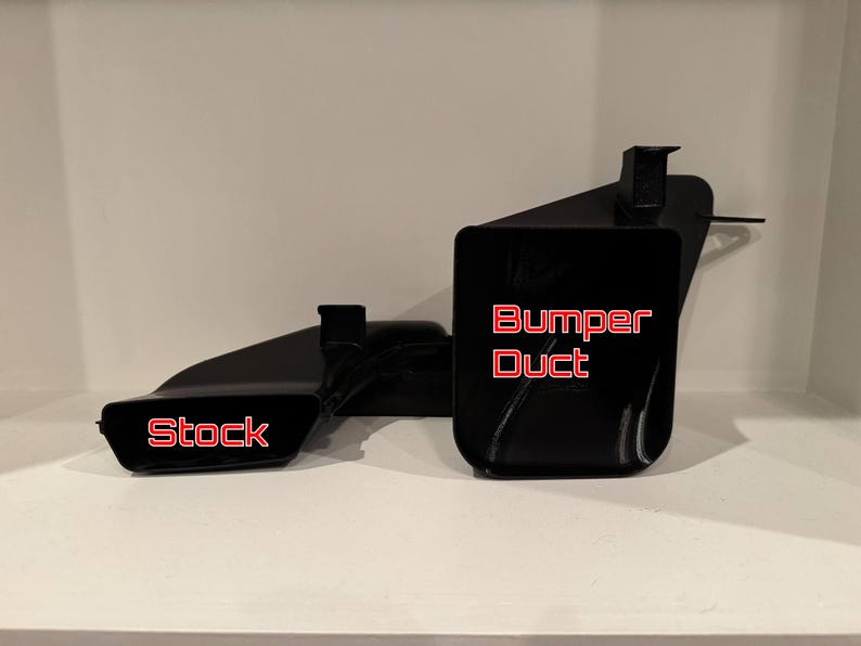 K&ouml;nnte beinhalten: Schwarze Autoteile mit den roten Aufschriften "Stock" und "Bumper Duct". Die Teile bestehen aus gl&auml;nzendem schwarzem Material und werden auf einer wei&szlig;en Oberfl&auml;che pr&auml;sentiert.