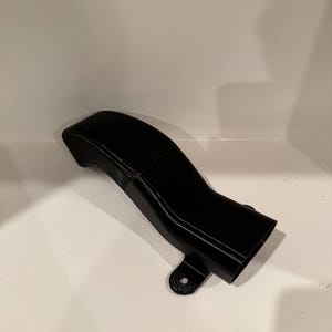 K&ouml;nnte beinhalten: Ein schwarzes, gebogenes Kunststoffteil mit einer rechteckigen &Ouml;ffnung und einem Befestigungsloch. Das Teil hat eine glatte, gl&auml;nzende Oberfl&auml;che und scheint 3D-gedruckt zu sein. Das Design weist eine allm&auml;hliche Kurve und ein ausgestelltes Ende auf.