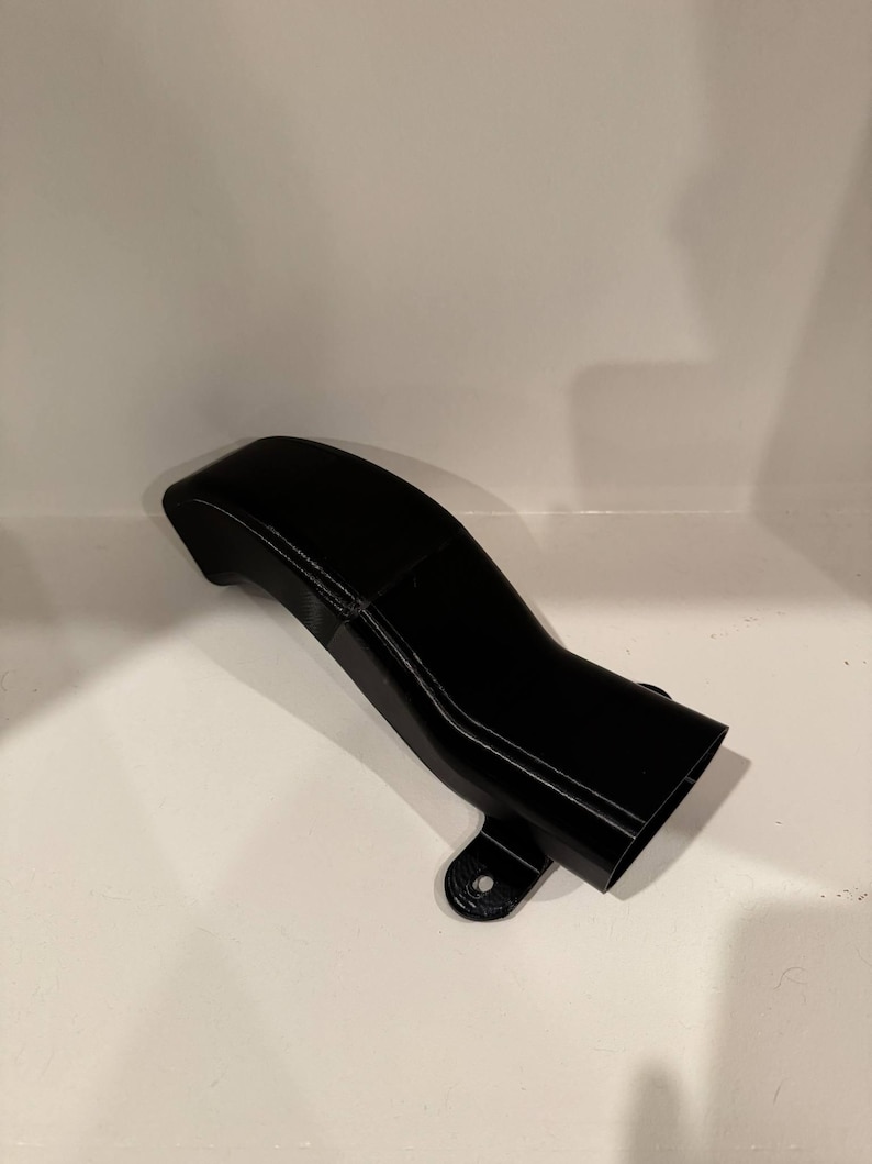 K&ouml;nnte beinhalten: Ein schwarzes, gebogenes Kunststoffteil mit einer rechteckigen &Ouml;ffnung und einem Befestigungsloch. Das Teil hat eine glatte, gl&auml;nzende Oberfl&auml;che und scheint 3D-gedruckt zu sein. Das Design weist eine allm&auml;hliche Kurve und ein ausgestelltes Ende auf.