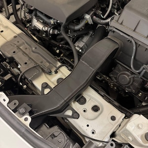 K&ouml;nnte beinhalten: Draufsicht auf einen Motorraum. Der Motor ist schwarz und grau, mit dem Text "turbo GR" sichtbar. Ein schwarzer Luftansaugkanal befindet sich in der Mitte, und die umgebenden Komponenten sind eine Mischung aus Schwarz, Grau und Wei&szlig;.