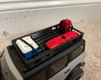 May include: A black metal roof rack with a white cooler, red gas cans, and red traction mats. The roof rack is mounted on a gray vehicle.